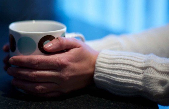 Hands holding mug of hot liquid, white jumper visible