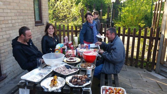 People smiling around a full picnic table of BBQ food