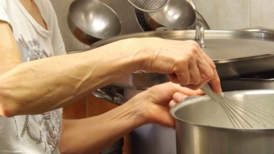 Hands using whisk to stir large saucepan