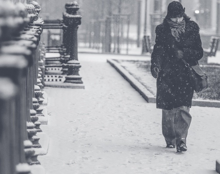 Woman wearing coat hat and scarf walking alone down snowy street