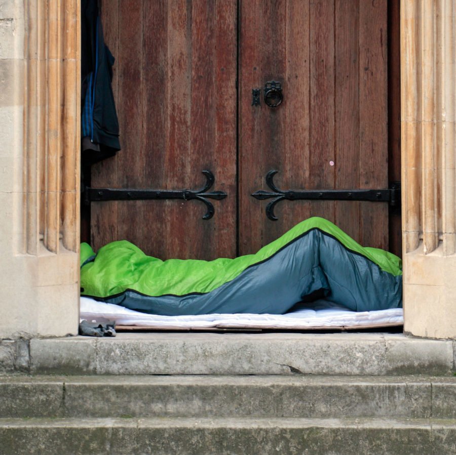 A man sleeping in a sleeping bag in a church doorway in London, UK