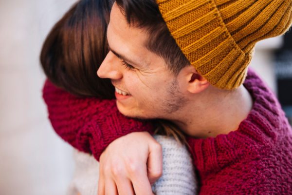 world homeless week website banner shows a young man with dark hair and stubble wearing a yellow beanie hat hugging a woman with brown hair