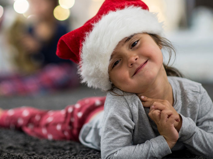 A little girl in a santa hat lying in the floor