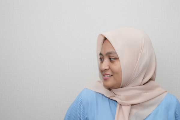 Photograph of a woman wearing a light pink headscarf and a light blue top facing to the left