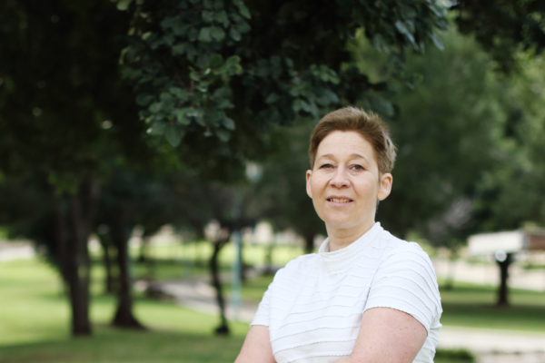 Photograph of a woman with short hair wearing a white top stood in a park