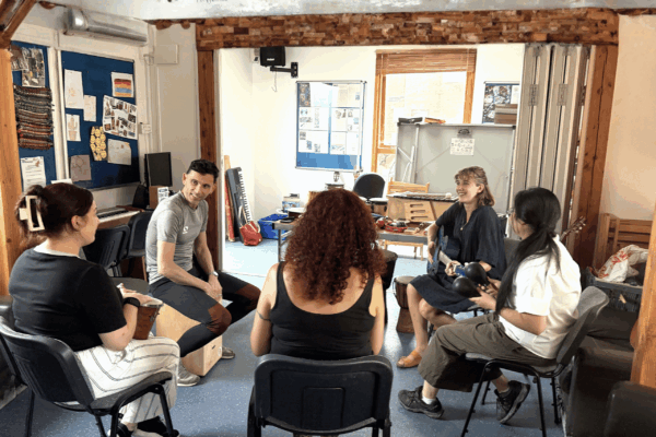 photograph on a music room were a session of music therapy is being held with 5 people sat in a circle on chairs each holding a different instrument
