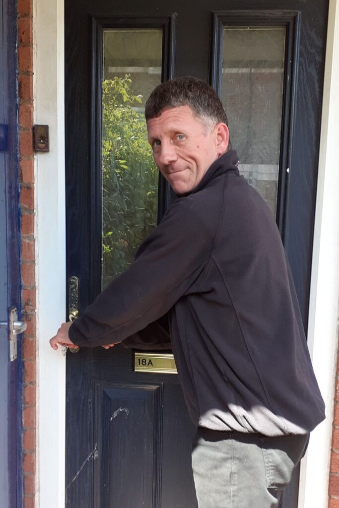 A man standing in front of the front door of a flat, ready to move in to start the rest of his life, leaving homelessness behind for good.