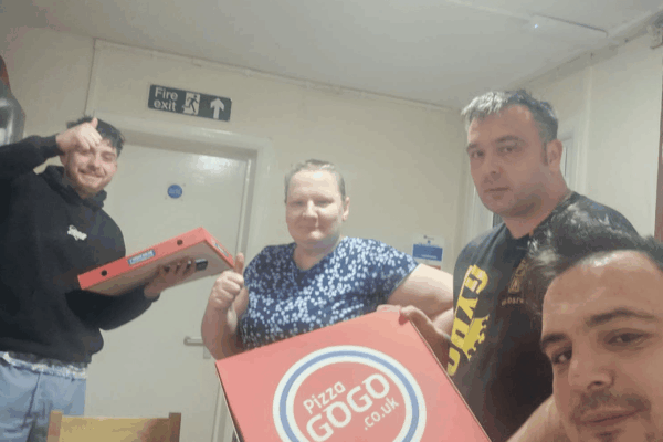 Photograph showing a group of people in a homeless scheme enjoying a takeaway pizza together